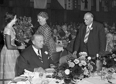 Feier zu Duttweilers 70. Geburtstag am 15.  August 1958: Adele Duttweiler, der Frau des Jubilars (rechts) werden Rosen überreicht (Foto Ernst Köhli)