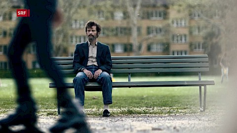 Joel Basman als gealterter Walter Stürm alleine auf einer anderen Parkbank im Bullingerhof